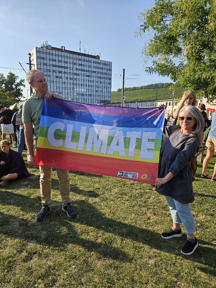 Zwei Teilnehmer*innen mit aufgehaltener Regenbogenfahne mit der Aufschrift "Climate" in der Mitte