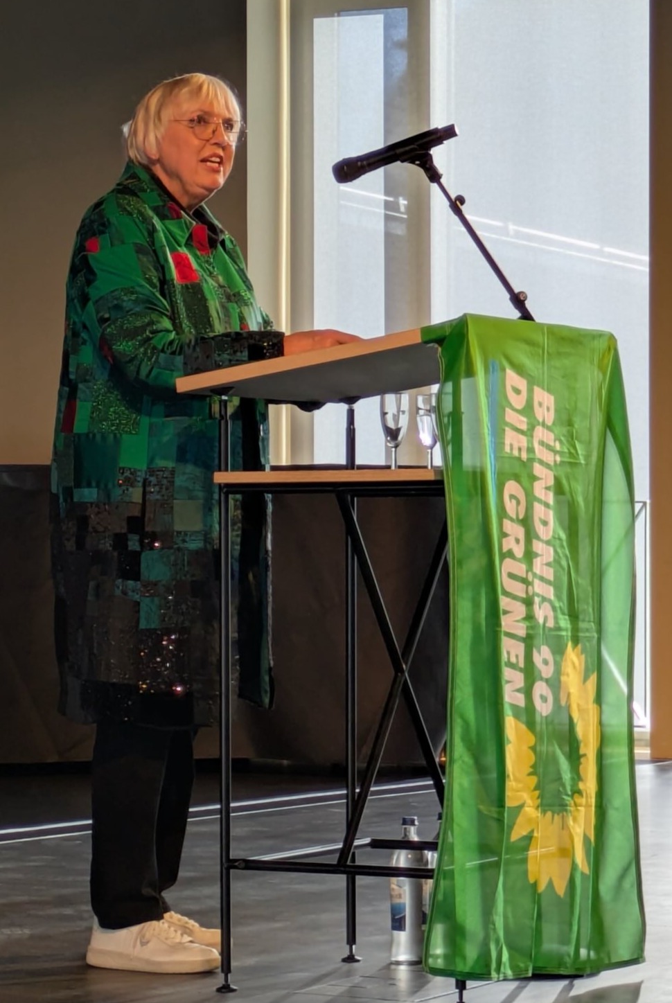 Claudia Roth hält eine Rede vor einem Pult mit einer grünen Flagge