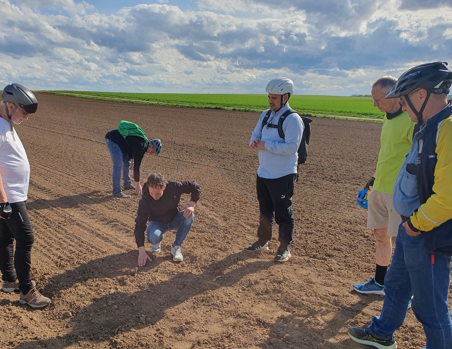 Markus Metzger mit den Radler*innen auf einem Acker und den Boden betrachtend.