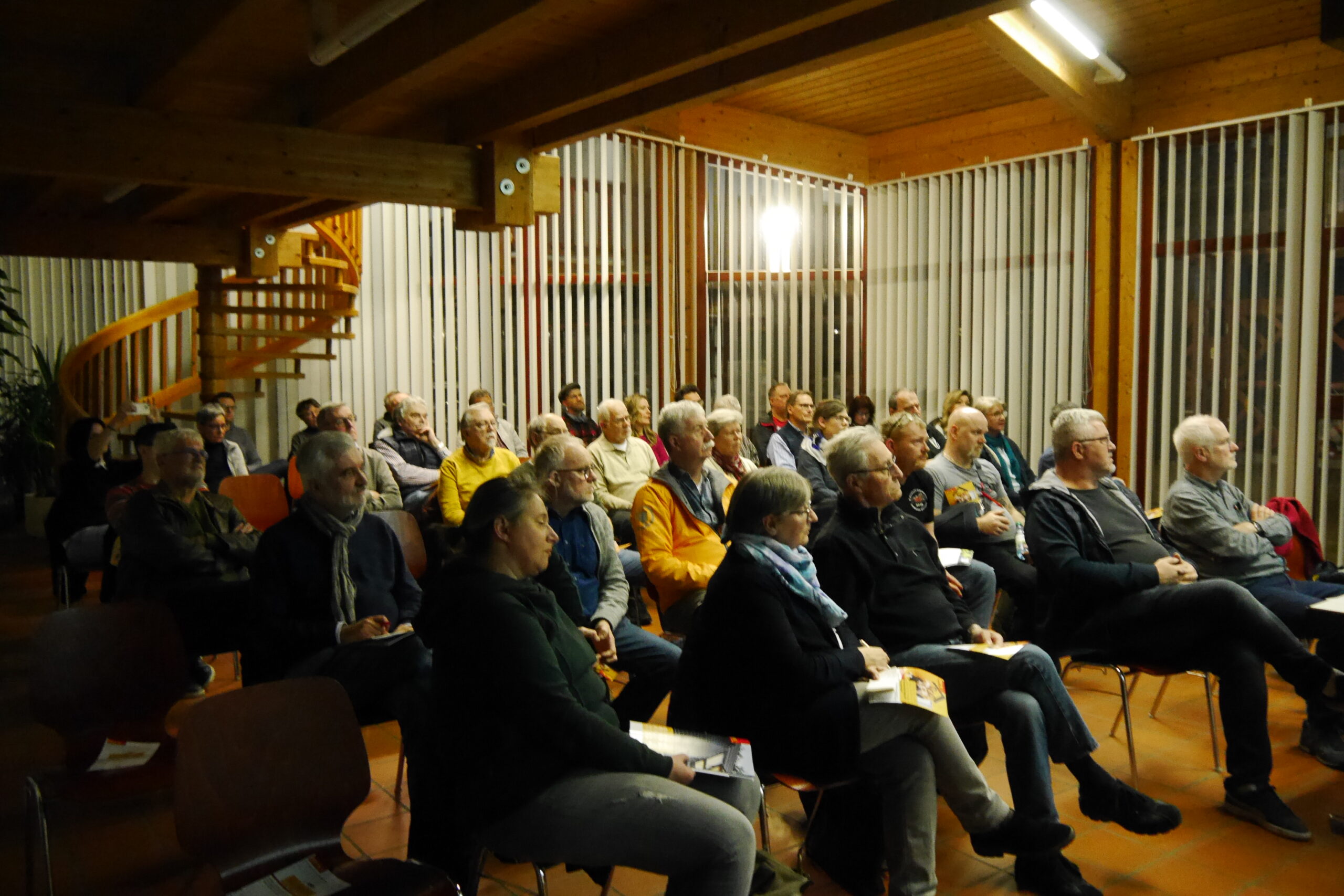 Die Gäste hören auf Stühlen sitzend konzentriert dem Vortrag zu