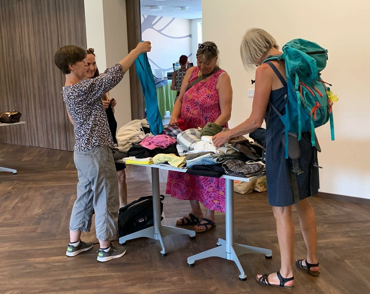 Drei Frauen stehen um eine Tisch herum und schauen sich die darauf liegenden Klamotten an
